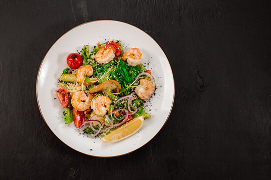 Tasty salad with shrimps, herbs and vegetables on black background