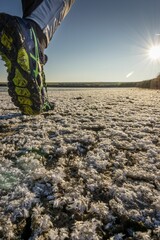 Vertical close-up of a person wearing boots walking on the snow-covered grass on a sunny day