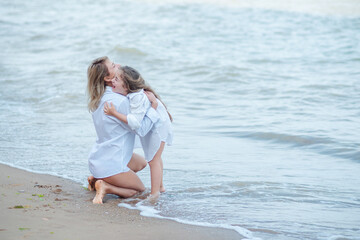 Fototapeta na wymiar Smiling young mother and beautiful daughter having fun on the beach with copy space. Lovely kid embracing her mom