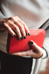 Beautiful black painted nails on woman's hand holding a red wallet. Winter manicure.