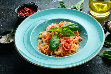 Pasta with chicken fillet, tomatoes and basil in a plate. Italian dish. On a black stone background.