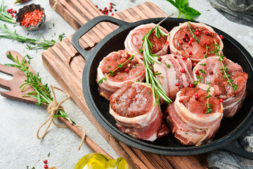 Raw meat medallions wrapped in bacon. in a pan, ready to cook. On a concrete background. Side view.