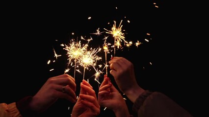 Hands of people with sparklers celebrating new year holiday at night. Beautiful bokeh lights background. New Year party, holiday concept