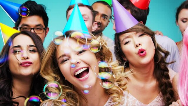 Diversity, dance and portrait of friends at party with colorful hats, bubbles and happy mood. Celebrate, youth and gen z people faces dancing together with smile for birthday in blue studio.