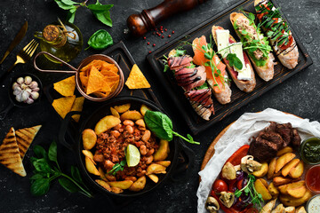 Food. Baked potatoes with meat and a set of sandwiches. On a black stone background.