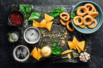 Two glasses of beer and salty beer snacks on a wooden tray. On a black stone background.