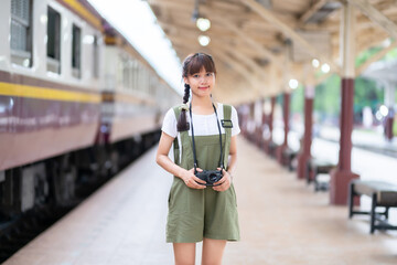 Portrait Young asian woman smiling tourist Traveler girl walking and with a holding the camera waits train travel journey is taken in railway platform Thailand, summer relax vacation Concept.