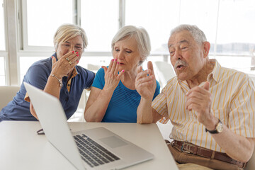 gruppo di tre anziani mandano saluti e baci allo schermo di un computer durante una videochiamta, ...
