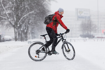 A man with a backpack rides a bike on a winter path, side view