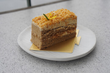 coffee almond crunchy cake on gold paper on white ceramic plate, on grey marble background, dessert, food, snack, copy space