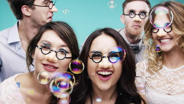Friends, party props and celebration in photobooth with bubbles and glasses on group together for comic, funny and crazy memory at social event. Men and women celebrate holiday in booth with a smile