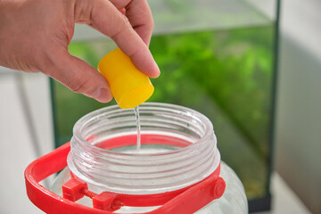 Close up of a hand adding fish tank water conditioner to fill freshwater aquarium. Fish tank...