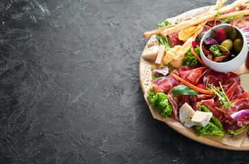 Antipasto Assortment of appetizers: cheese, prosciutto, salami, bacon, olives and capers on a wooden board. Top view. Free space for text.