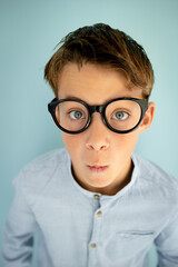 young cool boy with blue shirt, with big massive black glasses standing in front of blue background