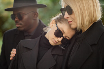 Mother and daughter embracing at outdoor funeral ceremony and grieving together lit by sunlight