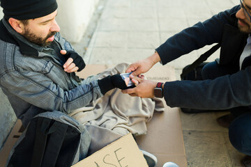 Fototapeta premium Concerned kind man giving money for food to a poor homeless man