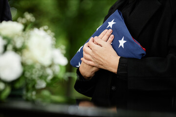 Woman holding American flag to chest at outdoor funeral ceremony for veteran, closeup - obrazy, fototapety, plakaty