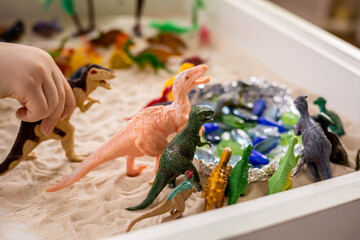 Closeup baby boy hands playing carnivorous and herbivorous dinosaurs with kinetic sand sensory box