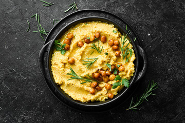 Hummus with chickpeas and rosemary in a black stone plate. Vegetarian food. Top view. On a black...