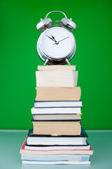 time to learn concept. chrome alarm clock on the top of high heap or stack of books on tha table...