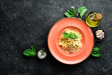 Pasta with chicken fillet, mushrooms, cheese and basil in a plate. Italian dish. On a black stone background.