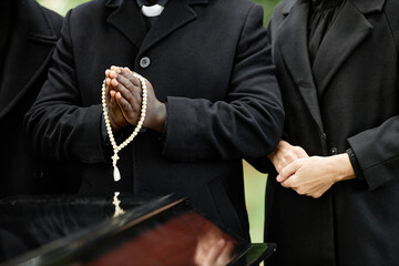 Close up of people wearing black at outdoor funeral ceremony with focus on rosary