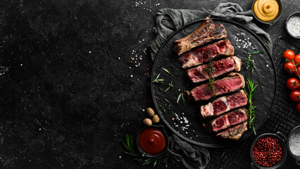 Veal steak on a bone. Juicy pieces of steak. Free space for your text. Top view. On a black stone background. - obrazy, fototapety, plakaty