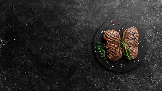 Grilled ribeye beef steak, herbs and spices on a dark table. Top view.