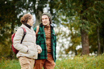 Waist up portrait of smiling young couple enjoying walk in autumn forest, copy space