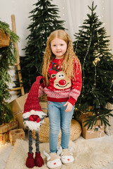 Child girl in stylish Christmas sweater with deer and comfortable home slippers near Xmas Tree....