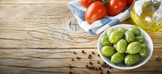 Green olives, cherry tomatoes, peppercorns and extra virgin olive oil on old wooden background,...