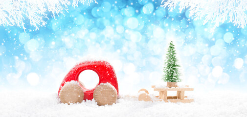 Red Wooden Car Pulling Sled with  A Christmas Tree in perspective on bright blue bokeh winter background with white snowy branches and falling snow.