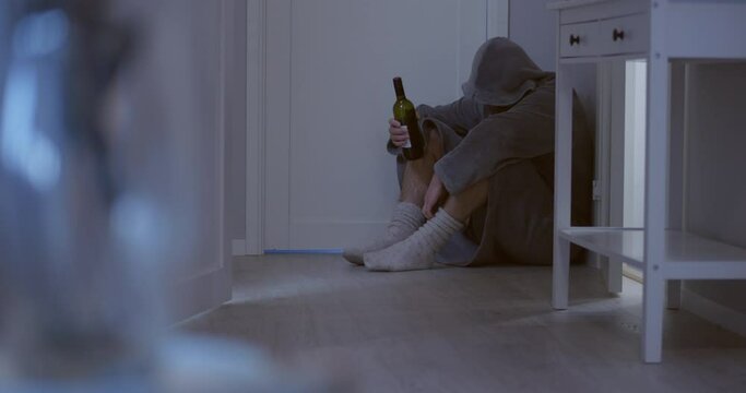 man huddled in corner of the room with bottle of wine