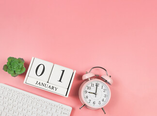  flat lay of computer keyboard, wooden calendar 01 January, pink vintage alarm clock 9 o'clock and succulent plant pot on pink background. First morning of new year.