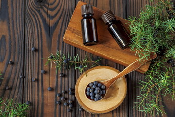 Fresh purple organic juniper berries in a wooden spoon and a bottle of oil on a wooden background top view