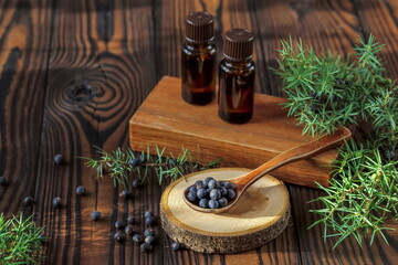 Fresh purple organic juniper berries in a wooden spoon and a bottle of oil on a wooden background