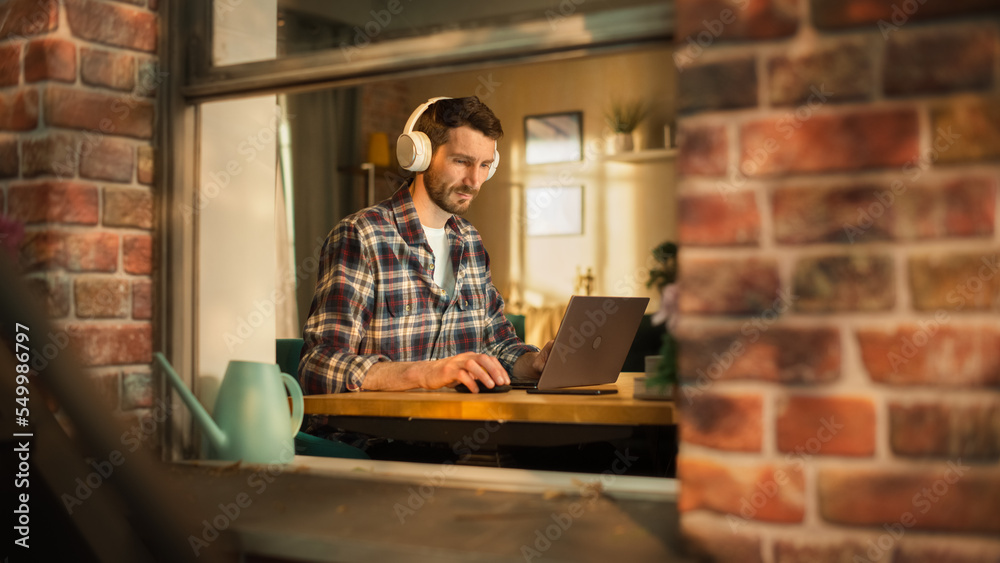Poster handsome caucasian man working on laptop computer while sitting behind his desk at home office. free