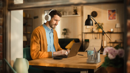 Thoughtful Man Using Laptop, Listens to Educational Audio Podcast in Headphones While Working...