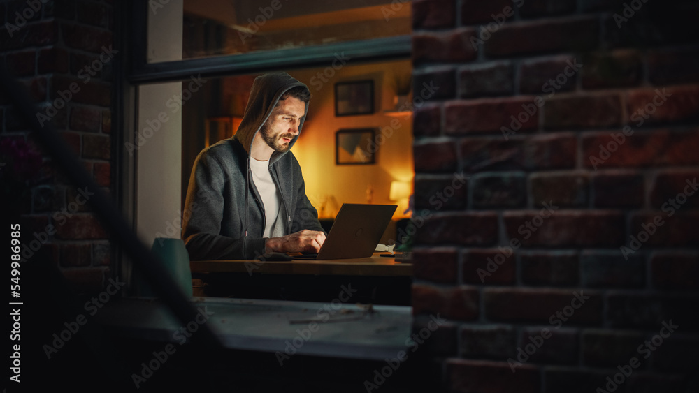 Aufkleber Professional Male Programmer Writing Code for Complex Project and Working Remotely on Laptop From Home Office. Freelance Software Engineer Designs App From Apartment. View From Outdoors into Window.