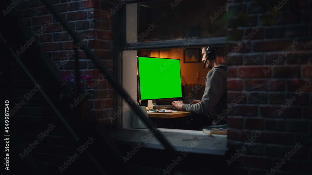 Poster Male Designer Using Desktop Computer with Green Screen Chroma Key Monitor. Remotly Working Manager Listening to Music or Podcast in Headphones, Freelancer Working at Night. Inside the Window Shot.