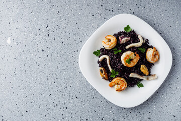 delicious black rice with shrimps and seafood on a gray stone background
