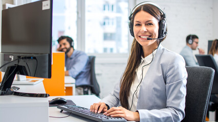 Friendly female helpline operator with headphones in call center.