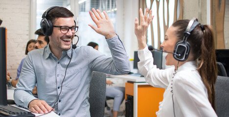 Customer service support operators giving high five to each other and celebrating successful completed task.