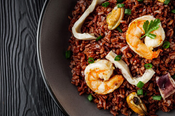 delicious red rice with shrimps and seafood on a black wooden rustic background
