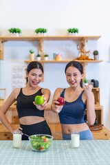  Choose red and green apple. Two young asian beautiful female lady friends in fitness costume choose healthy milk and salad. Say no to cholesterol and junk food.