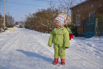 a baby is standing on the road in winter,A 2-year-old child is standing in the middle of the street on a beautiful sunny day in winter