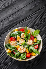 delicious fresh shrimp salad with orange and cherry tomatoes on a black wooden rustic background