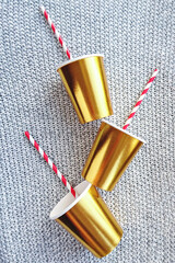 Gold-colored paper cups with striped straw on knitted background for Christmas party decorations, mockup