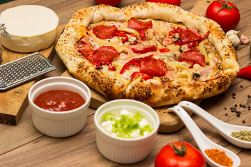 Tasty pizza with pepperoni, ham and peppers and pizza ingredients around the table
