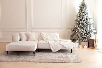 Comfortable couch with three cushions and a blanket standing in bright room interior with grey carpet in a modern interior. Modern interior living room with large light corner sofa and Xmas tree.	